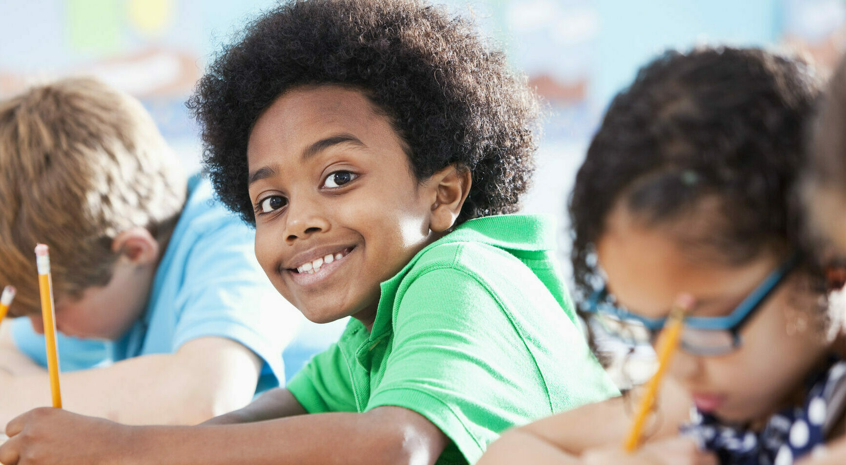 Multi-ethnic elementary school children writing in classroom. Focus on African American boy (8-9 years).